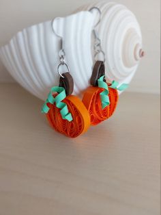 two orange and green earrings sitting on top of a white object next to a seashell