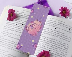 an open book with a cat on it next to pink flowers and purple ribbon,