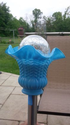 a blue glass vase sitting on top of a metal pole in front of a lawn chair