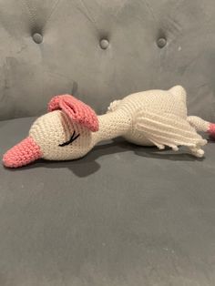 a crocheted white and pink stuffed animal laying on a gray couch with it's eyes closed