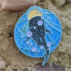 a blue and yellow plate sitting on top of sand next to a seashell with a shell in the background