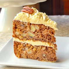 a slice of carrot cake on a plate with a pecan in the middle and white frosting