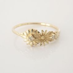 a yellow gold ring with three flowers and two diamonds on the side, sitting on a white surface