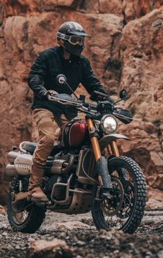 a man riding on the back of a motorcycle down a dirt road next to rocks