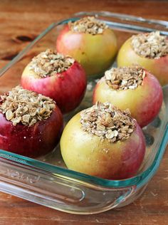 four apples in a glass dish with granola toppings on the top and bottom