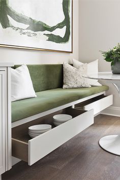 a green couch sitting under a painting next to a table with white plates on it