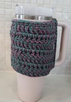 a crocheted coffee cup cozying in front of a white tile back splash