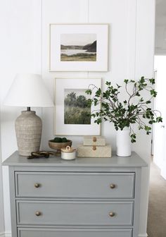 a dresser with some pictures on the wall and a plant sitting on top of it