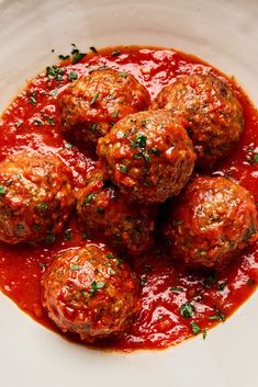 meatballs covered in marinara sauce and parsley on top of a white plate