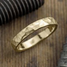 a gold wedding ring sitting on top of a wooden table next to a knife and pen