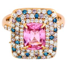 This enchanting ring boasts a central 1.51-carat cushion-cut pink sapphire, radiating elegance and charm. Surrounding the sapphire are three exquisite halos: the first halo features white round diamonds; second and third halos enhance the design with a harmonious blend of white, pink, and blue round diamonds—66 white diamonds (0.68 carats) 15 pink diamonds (0.18 carats) and 15 blue diamonds (0.16 carats). Adding a unique flair, 10 side-drilled diamonds weighing 0.97 carats elegantly dangle around the setting, creating a captivating movement. Crafted in 14k pink gold weighing 5.03 grams, this ring is a standout piece, perfect for any party or special occasion. Its eye-catching design, especially the dangling diamonds, ensures it will capture attention and admiration. Perfect for day and nig Color Diamond Ring, Ring Indian, Colored Diamond Rings, Blue Diamonds, Pink Diamonds, Gold Cocktail Ring, Gold Cocktail, Sapphire Stone, Color Ring