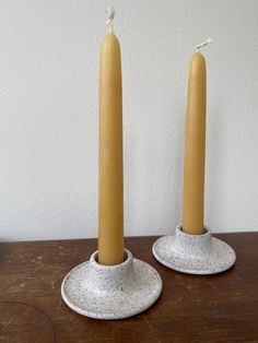 two yellow candles sitting on top of a wooden table next to each other with white speckles