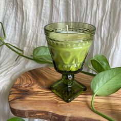 a green candle sitting on top of a wooden table next to some plants and leaves