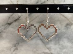 two heart shaped earrings hanging from a hook on a marble surface with holes in the middle