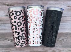 three different colored leopard print tumblers sitting next to each other on a wooden surface