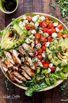 a salad with chicken, lettuce, tomatoes and avocado in it