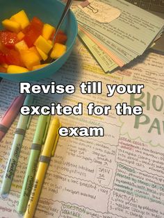 a bowl of fruit sitting on top of a table next to some pens and paper