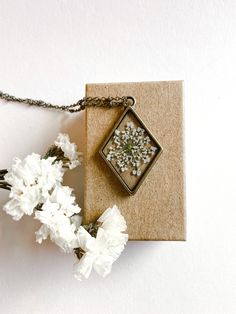 a small square pendant with tiny white flowers in it on a piece of brown paper