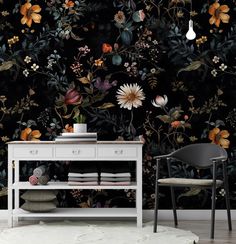 a white table sitting in front of a black wall with flowers and leaves on it