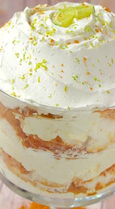 a layered cake with white frosting and limes on top is sitting in a glass dish