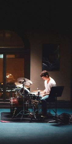 a man sitting in front of a drum set on top of a blue carpeted floor