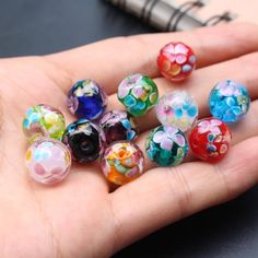 a hand holding seven colorful glass beads in it's palm, next to a pen