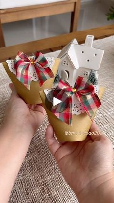 someone is holding two small boxes with bows on them, one in the shape of a house