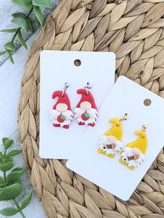 two christmas themed earrings sitting on top of a table next to a basket full of leaves