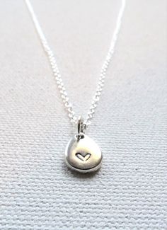 A tiny, delicate silver-plated teardrop hand stamped with a heart hangs from a delicate chain.  The lightweight teardrop is stamped by hand with a tiny heart.  Each silver plated textured teardrop charm (base metal of zinc alloy - lead and nickel free) measures 11 mm x 8 mm.  Due to the handmade nature of the necklace, no two are identical.  The irregular and slight imperfections are what set hand stamped jewelry apart from factory made pieces and offer a whimsical charm.  This is a wonderful gift for an anniversary, Valentine's Day, wedding, cancer support, everyday wear, or to celebrate the life or loss of an infant or loved one. Each piece is hand crafted when ordered so please allow 3-5 days for design creation.  Select chain length from drop down box.  An optional recycled glass bead Dainty Heart-shaped Hand Stamped Charm Necklace, Dainty Hand Stamped Heart Charm Necklace, Dainty Teardrop Heart Charm Jewelry, Dainty Teardrop Sterling Silver Charm Necklace, Dainty Sterling Silver Teardrop Charm Necklace, Sterling Silver Hand Stamped Heart Charm Necklace, Delicate Teardrop Sterling Silver Charm Necklace, Hand Stamped Heart Sterling Silver Charm Necklace, Dainty Teardrop Necklace For Everyday