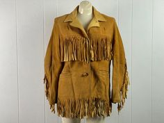 "Vintage 1950s tan Chamois leather buckskin fringe jacket. Cowgirl Cowboy western styled with leather button front and two pockets. Has smooth leather collar. Fully lined in silver Rayon. Front back and arm fringe, is 5\" and 6\" long. No Label, about a size large. Actual measurements are: 44\" at the bust, 39\" at the waist, 16.5\" shoulder seam to shoulder seam, 22\" shoulder seam to end of cuff and 29\" overall length. In good condition with some dirt near pockets, all over slightly discolore Western Leather Jacket With Fringe For Winter, Vintage Fitted Outerwear With Fringe, Fitted Vintage Outerwear With Fringe, Fall Leather Jacket With Fringe For Rodeo, Vintage Fall Outerwear For Ranch, Vintage Fall Outerwear For Western-themed Events, Leather Jacket With Fringe For Rodeo In Fall, Western Style Fringe Outerwear For Rodeo, Vintage Winter Leather Jacket With Fringe