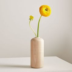 two yellow flowers in a wooden vase on a white countertop with light gray background