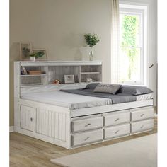 a white bed with drawers underneath it and a window in the backround behind it