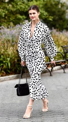 a woman in a polka dot dress is walking down the street with her handbag