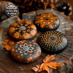 three painted rocks sitting on top of a tree stump next to autumn leaves and acorns