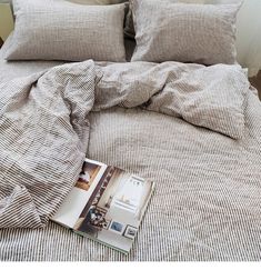 an open book is laying on the bed with two pillows and covers in front of it