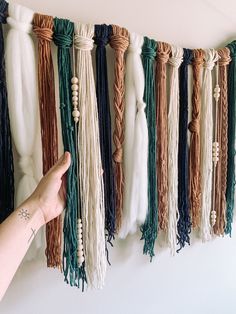 a hand is pointing at some tassels hanging on the wall