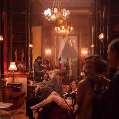 a group of people sitting around in a living room with chandelier above them