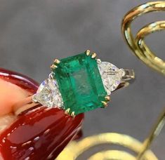 an emerald and diamond ring being held by someone