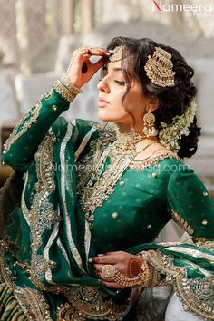 a woman in a green and gold bridal outfit looking off to the side with her hands on her head