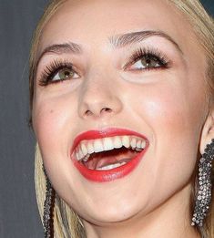 a close up of a woman with red lipstick and big earrings on her face smiling