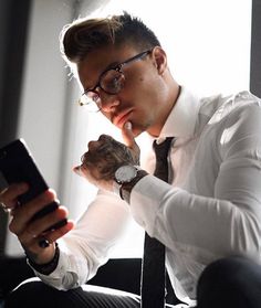 a man wearing glasses and a white shirt is looking at his cell phone while sitting in a chair