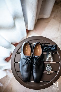 a pair of black shoes sitting on top of a wooden table next to a watch