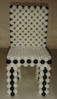 a chair made out of plastic balls and black and white beads is shown in front of a beige wall