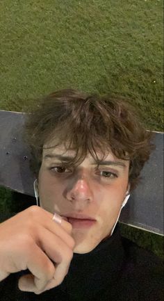 a young man with earphones on sitting next to a skateboard