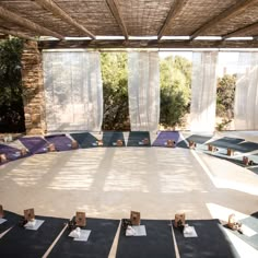 a large round table with chairs around it in the middle of an outdoor area that has curtains on both sides