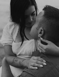 a man and woman kissing each other while sitting on the ground in black and white