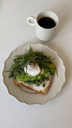 a white plate topped with an open face sandwich and a cup of coffee next to it