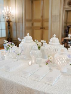 there are many white vases on the table with place cards in front of them