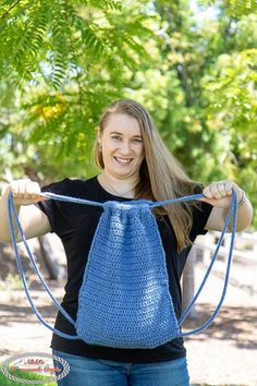 a woman holding up a blue crocheted bag in front of her face and smiling