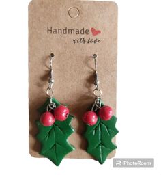 pair of earrings with holly leaves and red berries on the earwires, hanging from a card